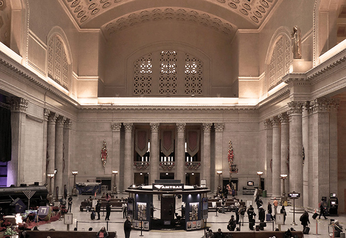 Rail passengers in a large room with high ceilings.