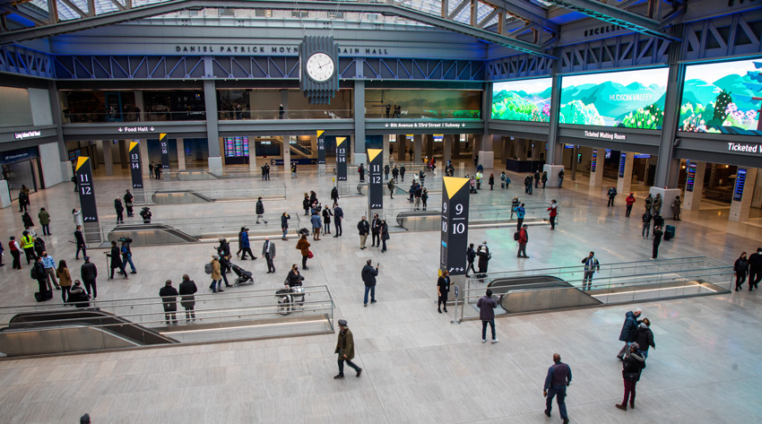 People walking in a large, open room with escalators leading to a lower level.