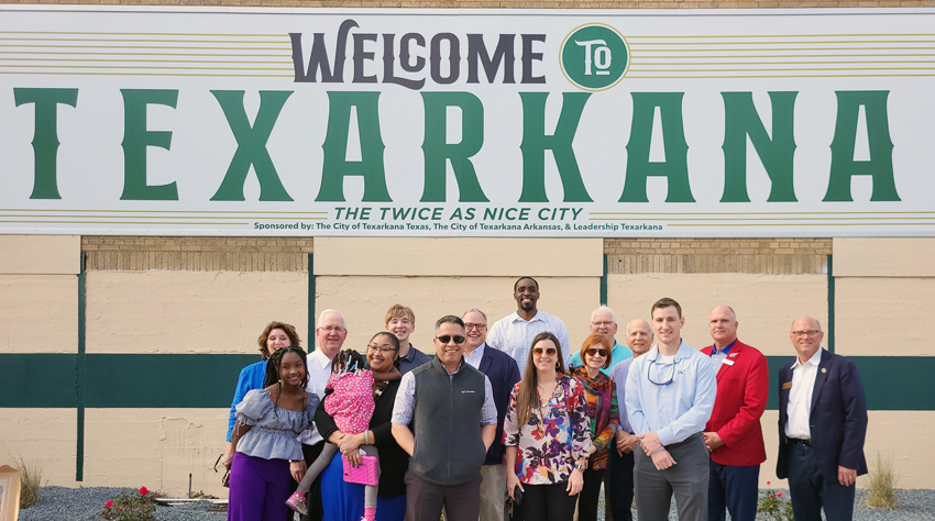 A group poses for a picture before a mural.