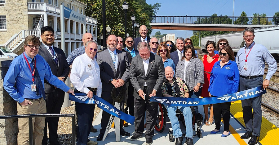 A group of dignitaries cuts a ribbon on a train platform.